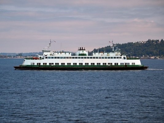 WSDOT ferry traveling between West Seattle ad Vashon Island with green hillside in the background