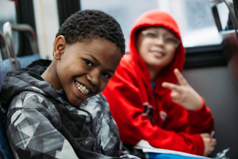 Two elementary-aged children smiling into the camera while riding a King County Metro bus.