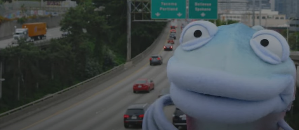 Sal the Salmon in front of the highway with cars in the background.