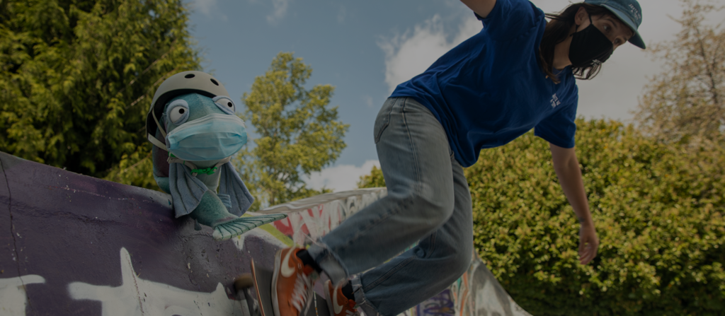 A woman on a skateboard at a skate park in Seattle, while Sal the Salmon looks on